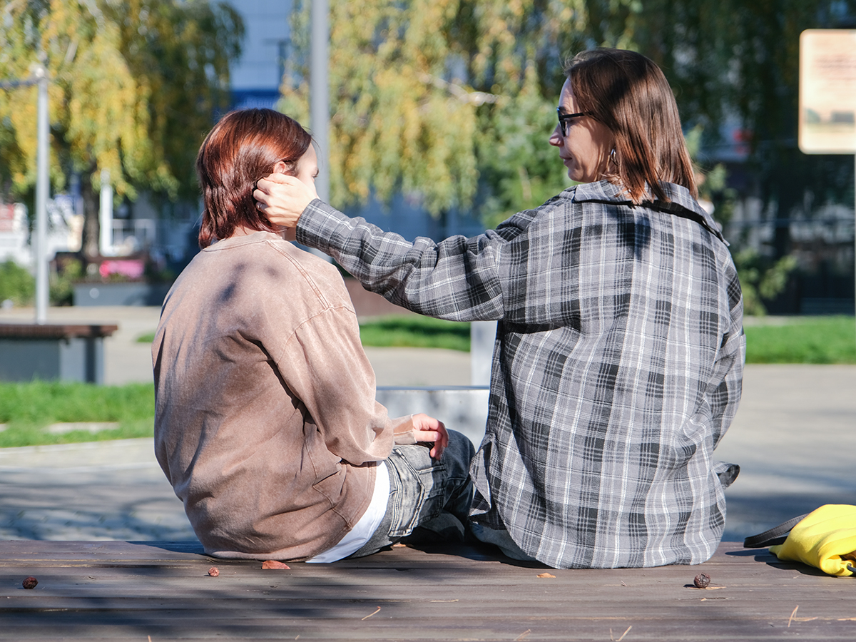 Two women sitting together on a bench, one resting a hand on the other's shoulder